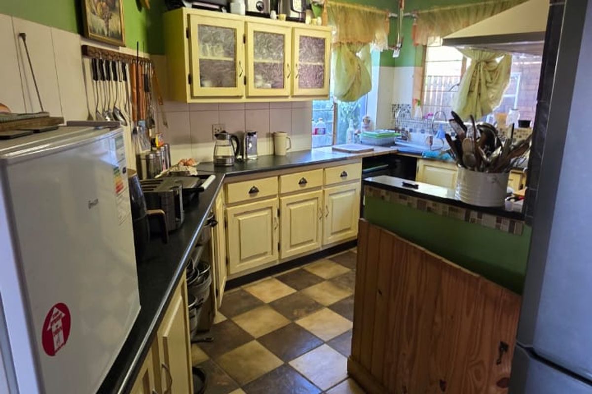 A dated kitchen featuring built-in cabinetry, tiled flooring, and a tiled backsplash, showing signs of ceiling water damage and general wear.