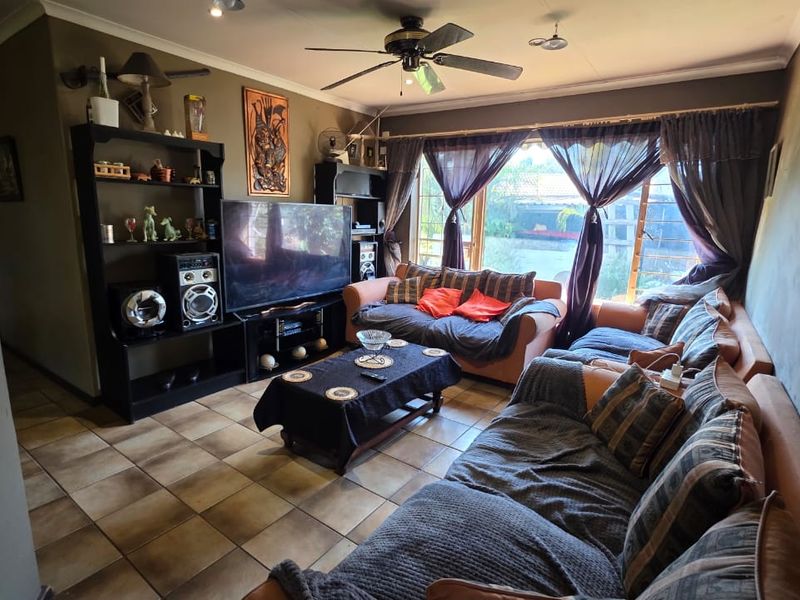 A comfortable living room featuring tiled flooring, a ceiling fan, and large sliding glass doors that provide natural light and garden access.