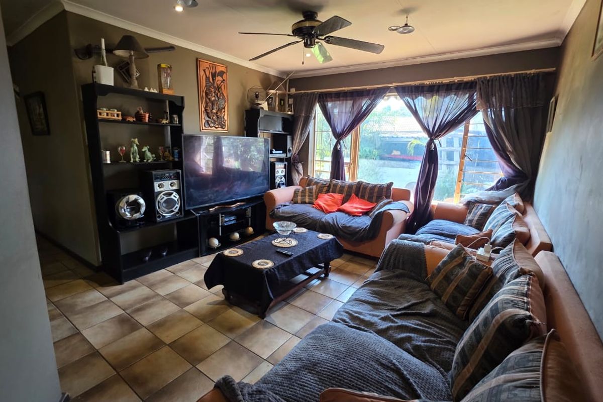 A comfortable living room featuring tiled flooring, a ceiling fan, and large sliding glass doors that provide natural light and garden access.