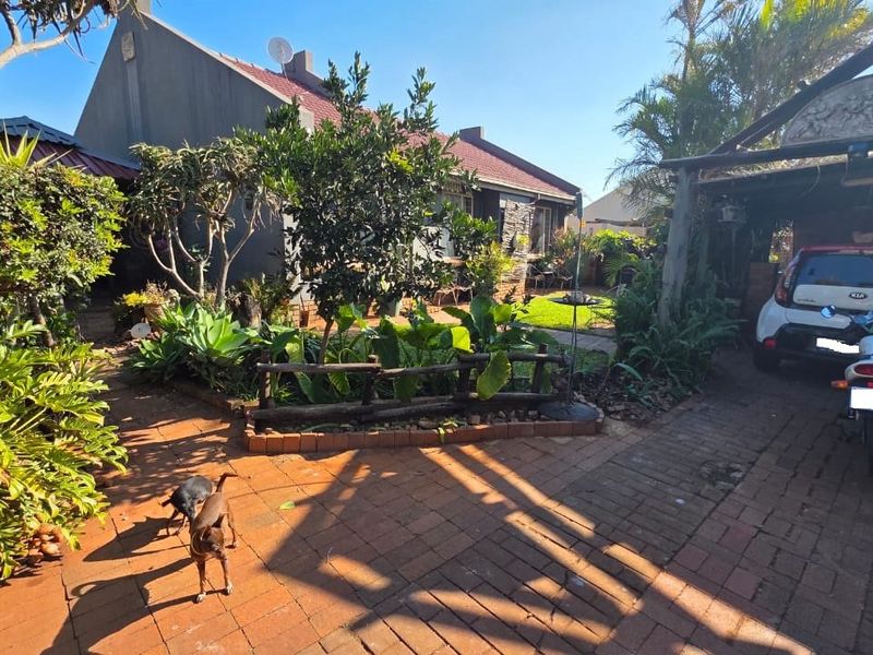 Front exterior view of the property featuring a brick paved driveway, a covered carport, and a well-established landscaped garden area.