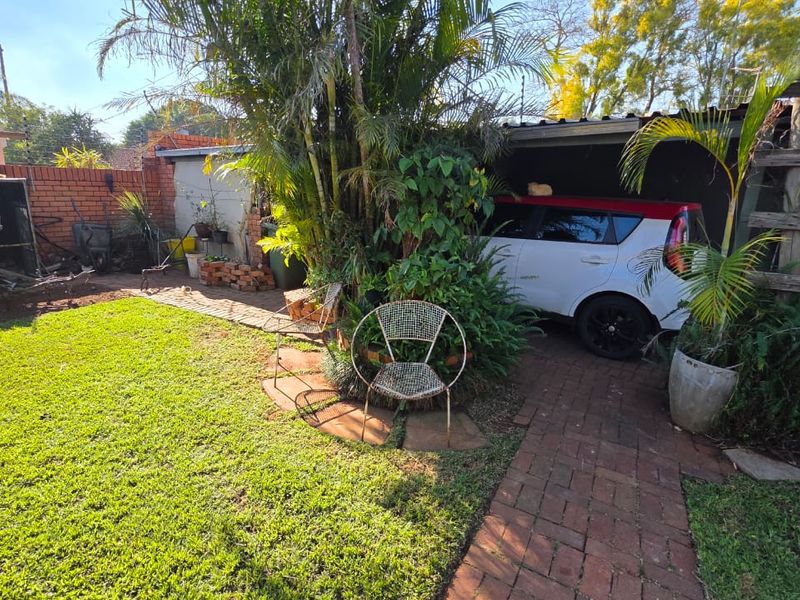 A residential garden area featuring a brick paved pathway, established landscaping, and a covered carport structure.