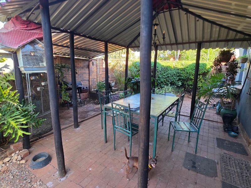 A covered outdoor patio area featuring brick paving, a corrugated metal roof, and a decorative mosaic wall section.