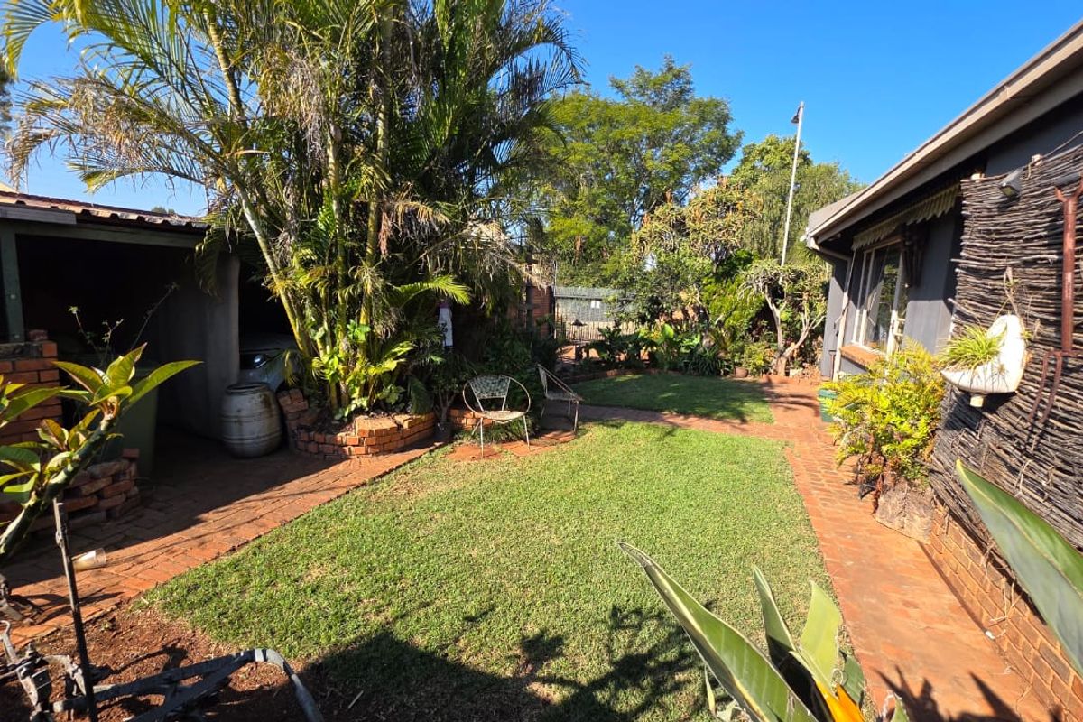 A rear garden area featuring a lawn, brick pathways, and a covered carport structure.