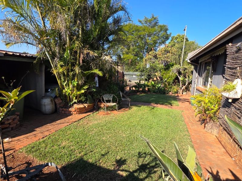 A rear garden area featuring a lawn, brick pathways, and a covered carport structure.