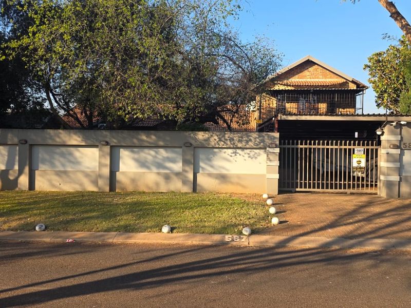 Front elevation of a residential property featuring a paved driveway, secure metal gate, and a perimeter wall with integrated lighting.