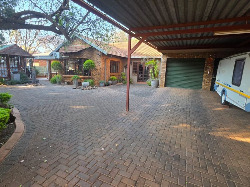 Front exterior view featuring a spacious brick-paved driveway, a covered carport, and a brick-built house with a tiled roof.