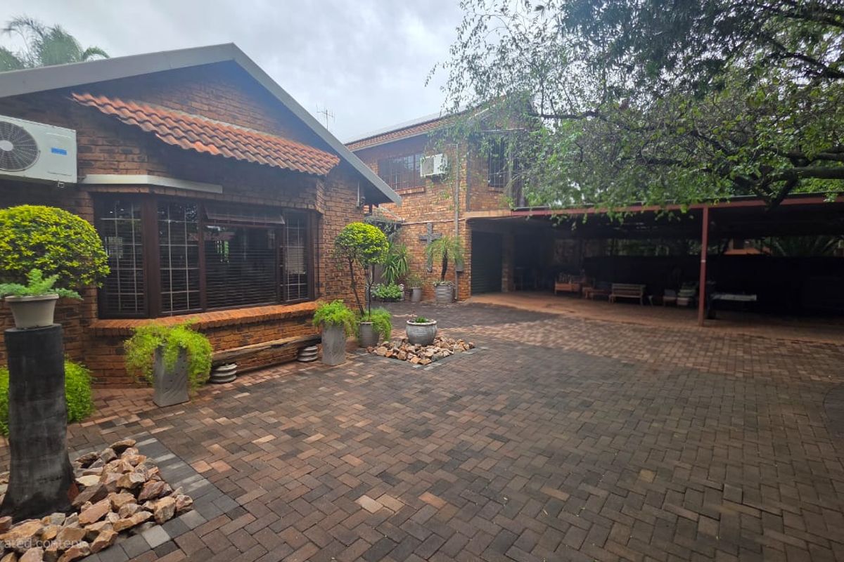 A spacious rear courtyard featuring a brick facade, paved driveway, and a covered carport area, providing ample space for parking and outdoor utility.