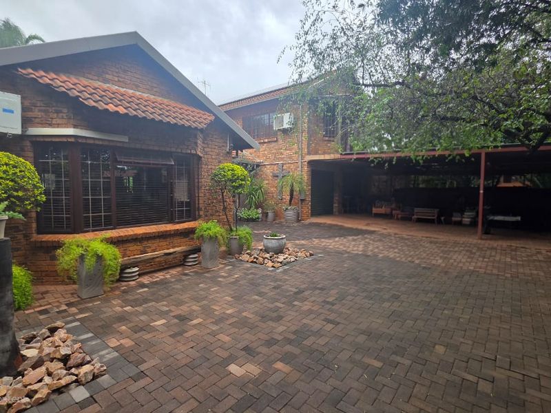 A spacious rear courtyard featuring a brick facade, paved driveway, and a covered carport area, providing ample space for parking and outdoor utility.