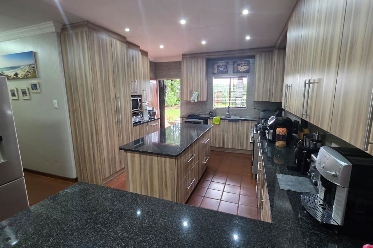 A well-appointed kitchen featuring modern wood-grain cabinetry, granite countertops, a central island, and tiled flooring with direct access to the rear garden.