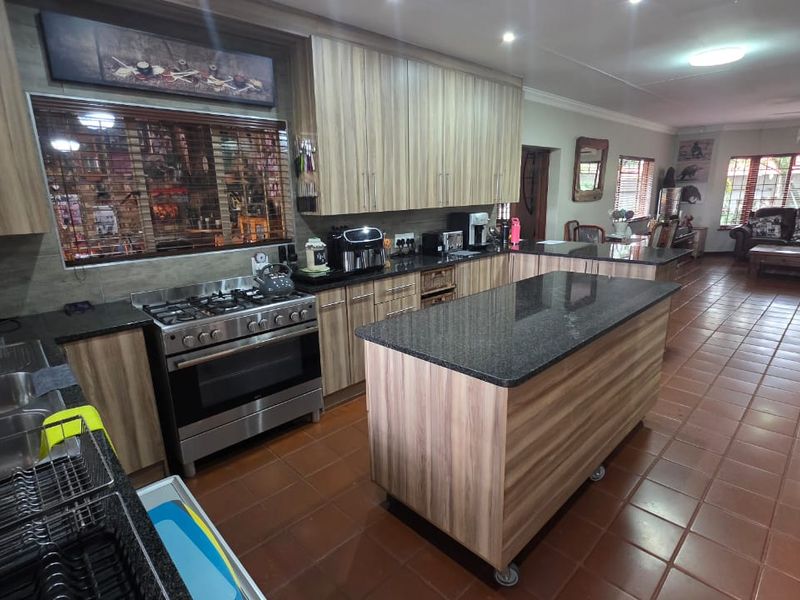 Spacious open-plan kitchen featuring wood-finish cabinetry, granite countertops, a central island, and a gas stove, flowing into the adjacent living area.