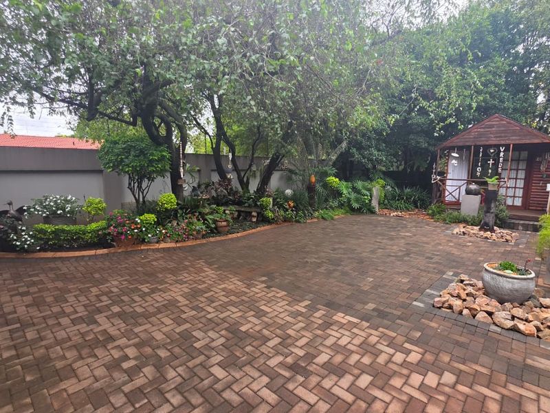 A well-maintained rear garden featuring paved flooring, established trees, landscaped garden beds, and a charming wooden gazebo structure.
