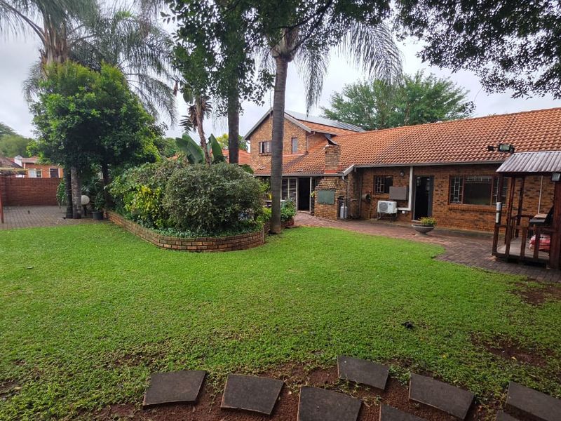 Spacious rear garden featuring a well-maintained lawn, paved patio area, brick facade, and established landscaping.
