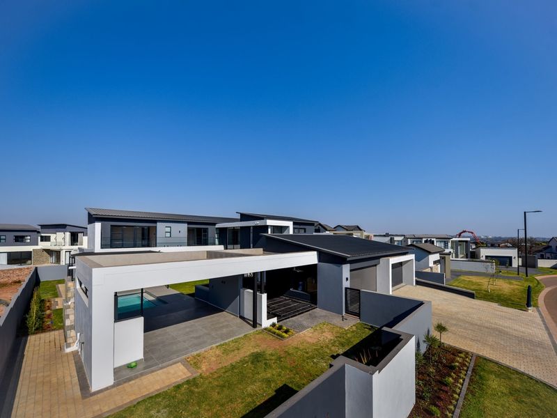 Aerial view of a modern residential property featuring a paved driveway, covered patio, swimming pool, and well-maintained landscaped garden areas.