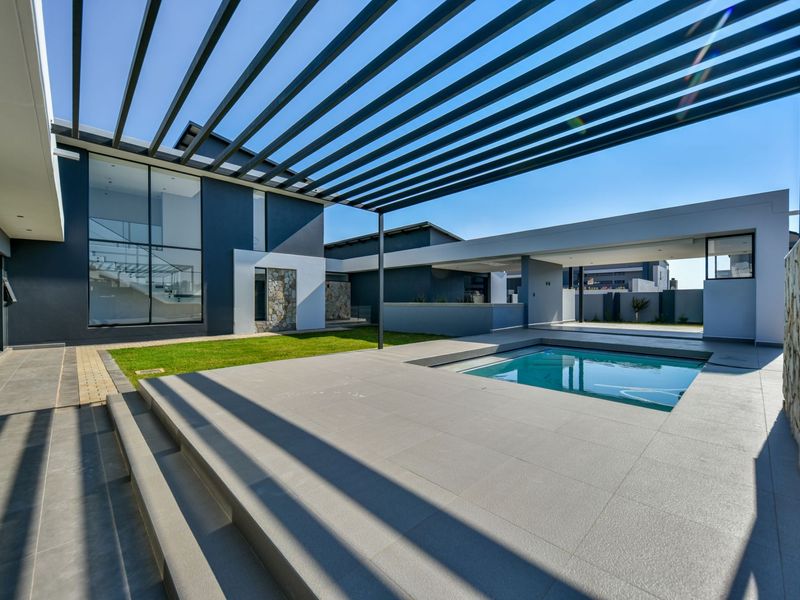 Modern outdoor entertainment area featuring a swimming pool, tiled patio, and a sleek pergola structure, set against a contemporary architectural facade.