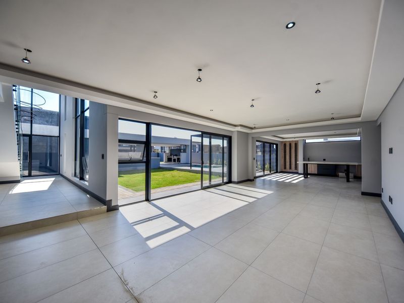 Spacious open-plan living area featuring large format floor tiles, recessed lighting, and expansive sliding glass doors opening to the rear garden and pool area.
