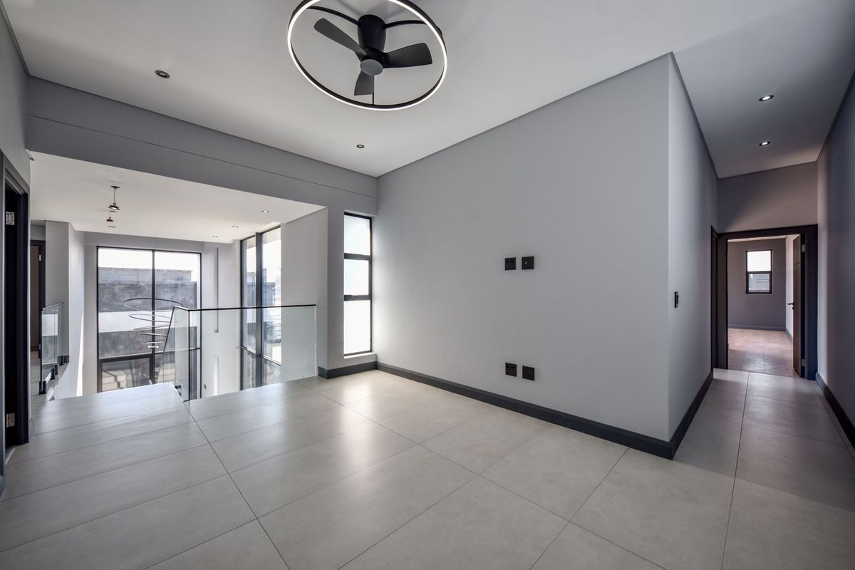 A bright, modern, and spacious open-plan living area featuring sleek tiled floors, a contemporary ceiling fan, and a glass balustrade overlooking the lower level.