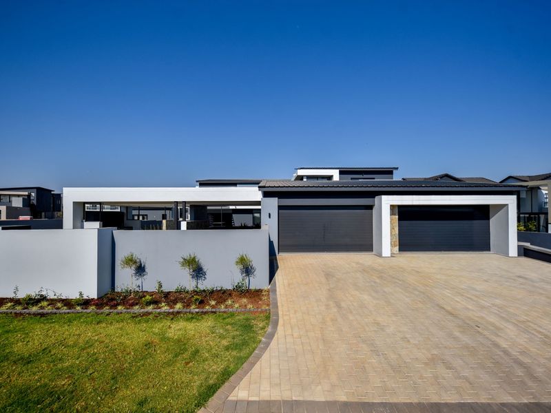 Modern contemporary house exterior featuring a double garage, paved driveway, and clean architectural lines with a well-maintained front garden.