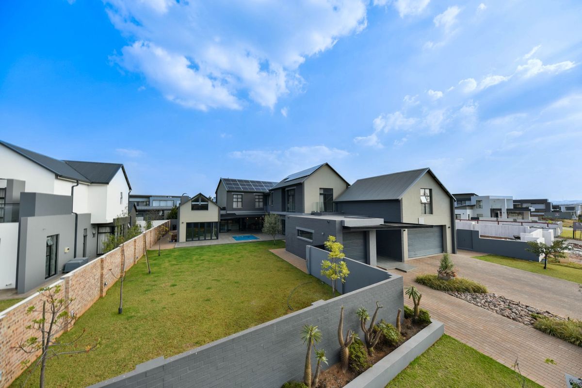 An elevated view of a modern residential property featuring a spacious lawn, swimming pool, double garage, and solar panel installation on the roof.