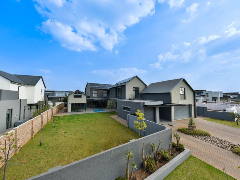 An elevated view of a modern residential property featuring a spacious lawn, swimming pool, double garage, and solar panel installation on the roof.