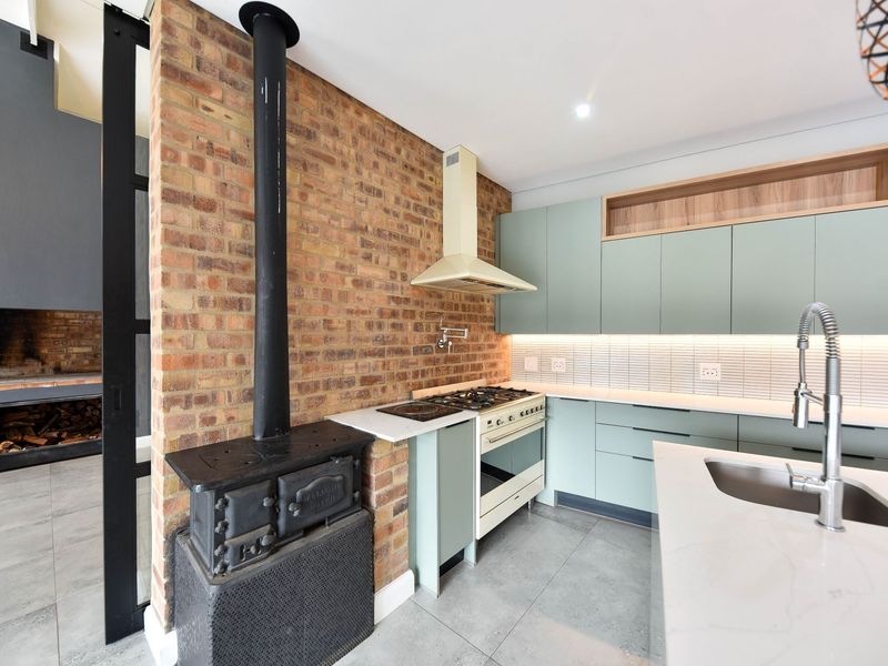 Modern kitchen featuring sage green cabinetry, stone countertops, a gas stove, and a striking exposed brick wall with a built-in wood-burning stove.