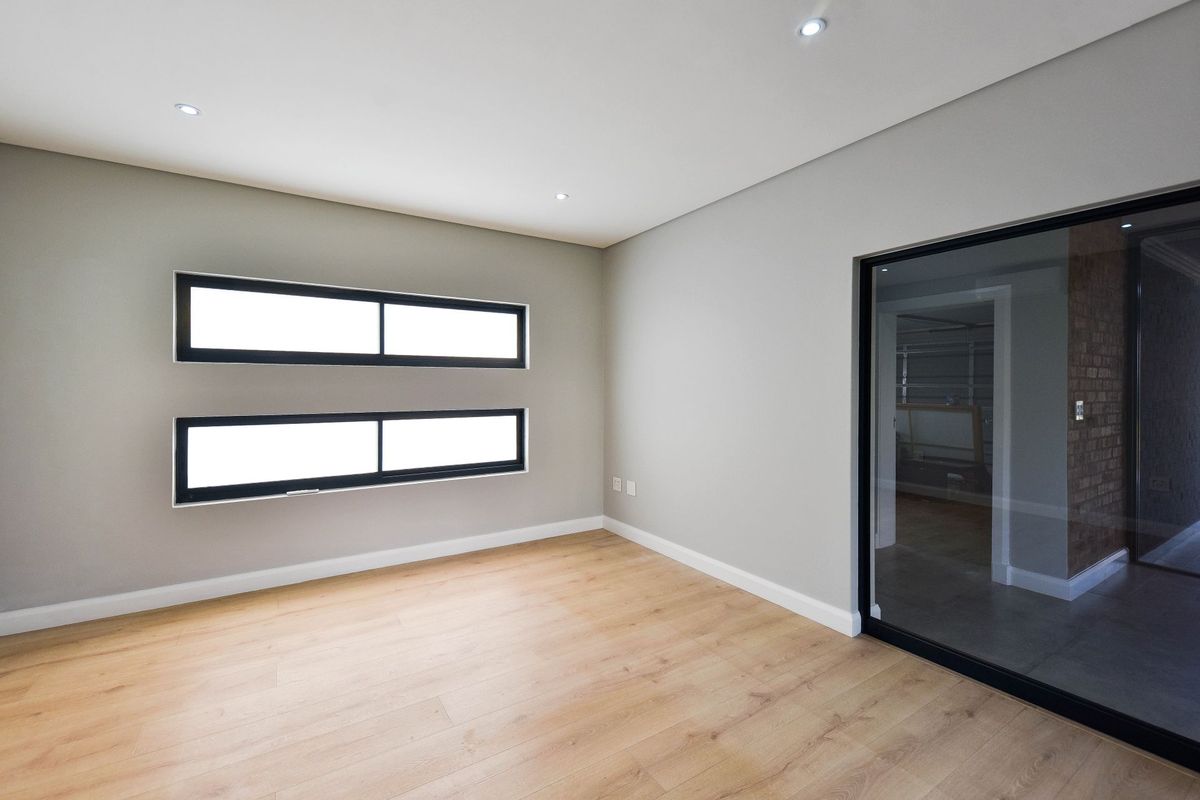 A bright, modern, and empty bedroom featuring light wood-look laminate flooring, recessed ceiling lighting, and contemporary black-framed windows and sliding glass door.