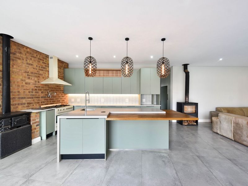 Modern open-plan kitchen and living area featuring a central island, exposed brick wall, and two wood-burning stoves, finished with contemporary cabinetry and tiled floors.