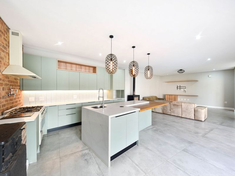 Modern open-plan kitchen and living area featuring a central island, stone countertops, gas stove, exposed brick accent wall, and a sleek freestanding fireplace.