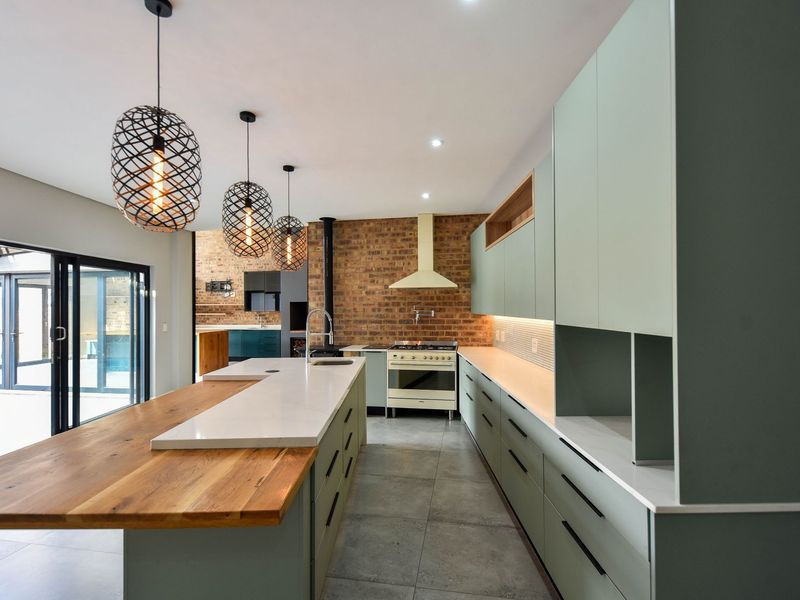 Modern kitchen featuring sage green cabinetry, stone countertops, a timber breakfast bar, and an exposed brick wall with a gas stove.