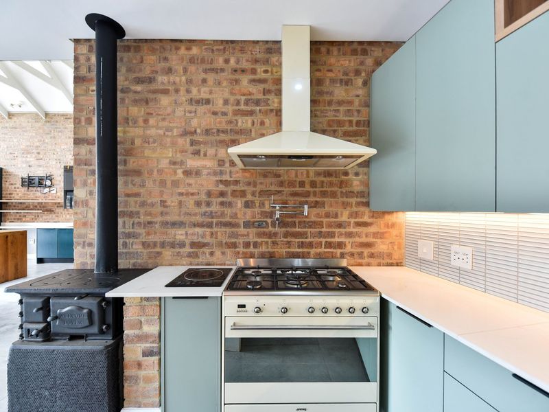 Modern kitchen featuring a striking exposed brick wall, integrated cabinetry, stone countertops, and a professional-style gas range cooker with a wood-burning stove.