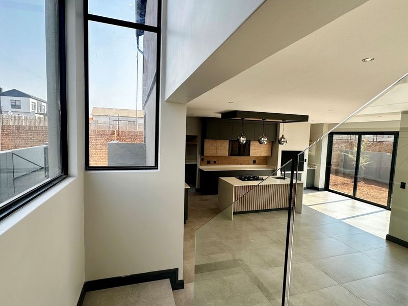 Modern open-plan living area featuring a sleek kitchen with a central island, tiled floors, and large windows providing ample natural light.