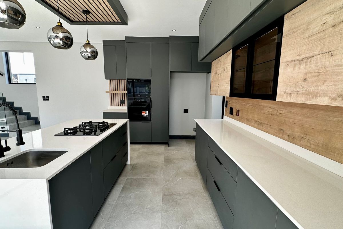 Modern kitchen featuring dark cabinetry, light wood accents, quartz countertops, a central island with a gas cooktop, and high-end integrated appliances.