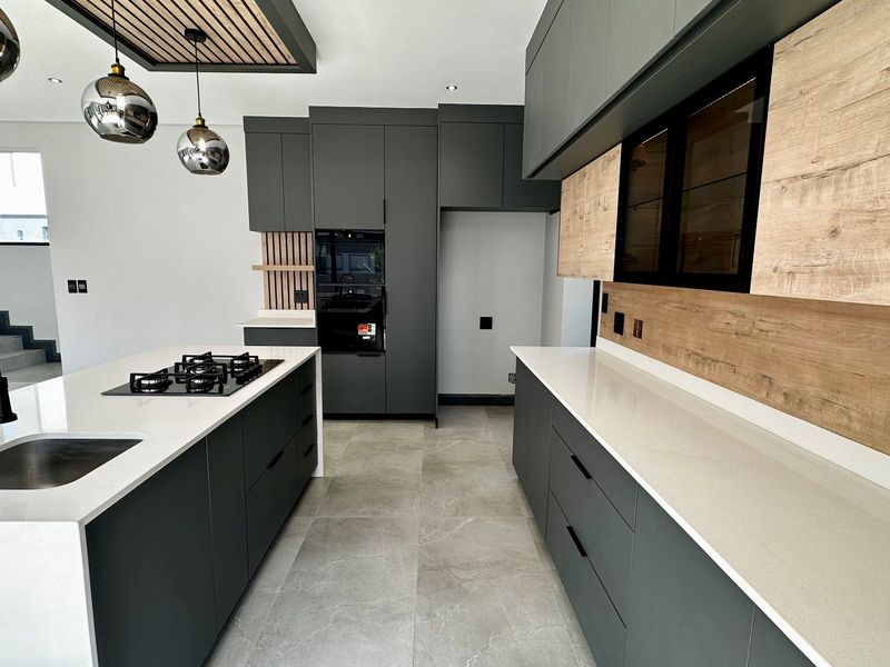 Modern kitchen featuring dark cabinetry, light wood accents, quartz countertops, a central island with a gas cooktop, and high-end integrated appliances.