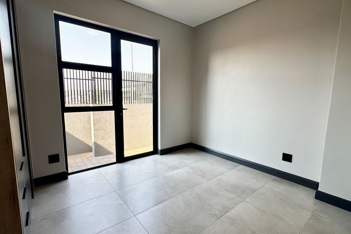 A bright, modern bedroom featuring large format floor tiles, a built-in cupboard, and a glass door providing access to an outdoor area.