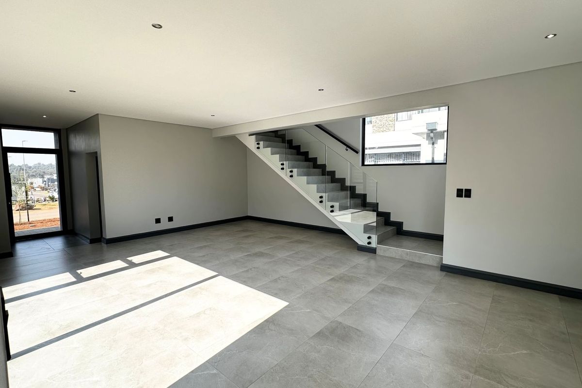 Spacious, modern open-plan living area featuring large format floor tiles, recessed lighting, and a contemporary staircase with a glass balustrade.
