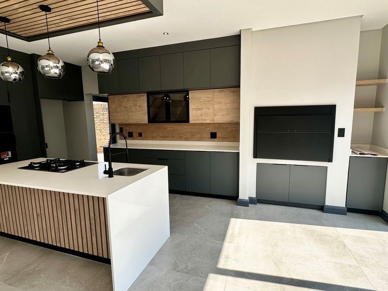 Modern kitchen featuring a large island with gas hob, sleek dark cabinetry, timber accents, and a built-in indoor braai area.