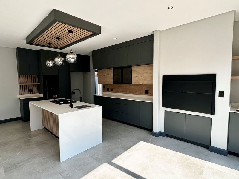 Modern kitchen featuring a central island, sleek dark cabinetry with wood accents, stone countertops, integrated gas hob, and a built-in fireplace.