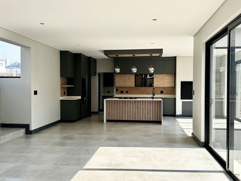 Modern open-plan kitchen featuring sleek dark cabinetry, a timber-accented island, and large sliding doors leading to the exterior, finished with high-quality tiled flooring.