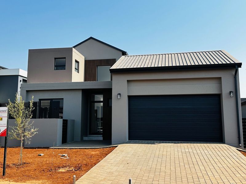 Modern double-storey residential home featuring a contemporary facade, metal roofing, and a paved driveway leading to a double garage.