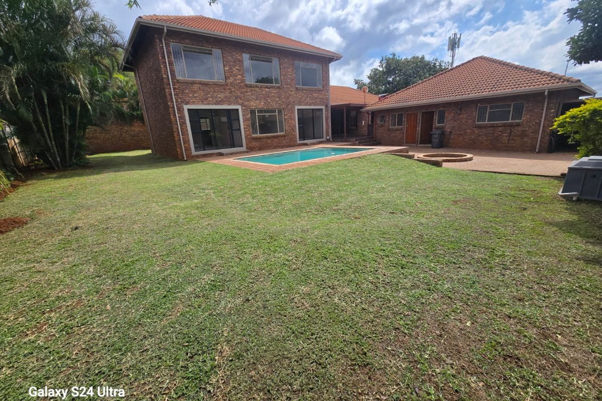 Rear view of a double-story brick house featuring a swimming pool, paved patio area, and a built-in fire pit set within a spacious garden.