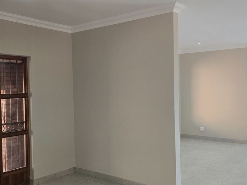 A bright and spacious open-plan living area featuring neutral walls, tiled flooring, and modern recessed lighting, offering a versatile blank canvas.