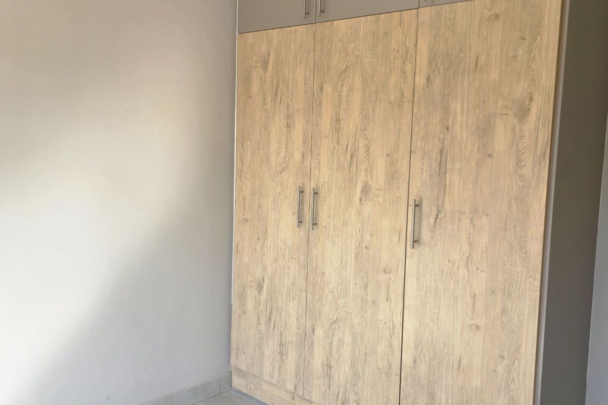 A clean bedroom space featuring modern wood-finish built-in wardrobes with overhead storage and neutral tiled flooring.