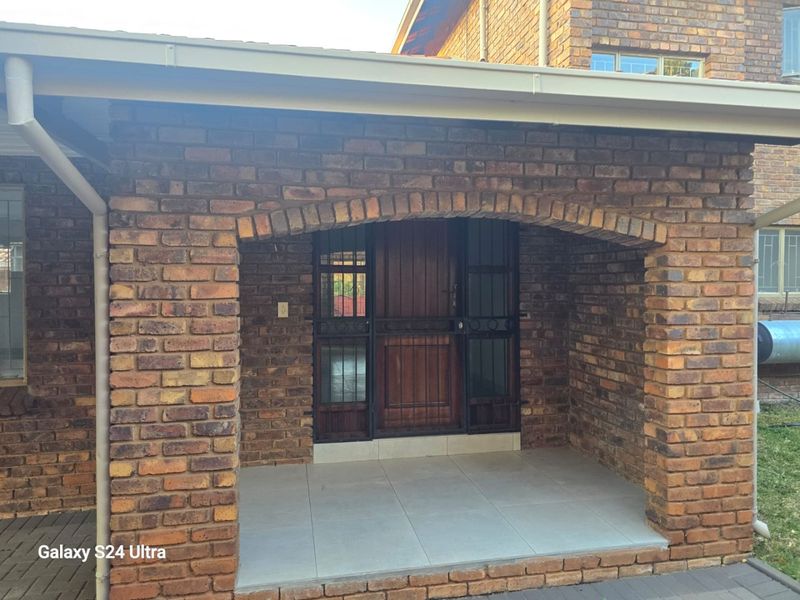 A covered entrance porch featuring a classic face brick archway, tiled flooring, and a solid timber front door with integrated security gate.