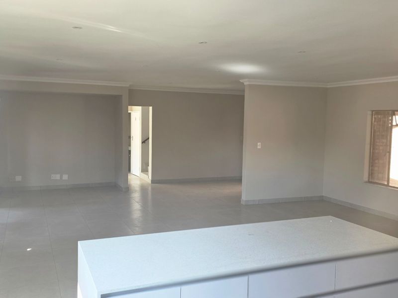 Spacious open-plan living area featuring neutral tiled flooring, recessed downlighting, and a central kitchen island, offering a versatile blank canvas for interior design.
