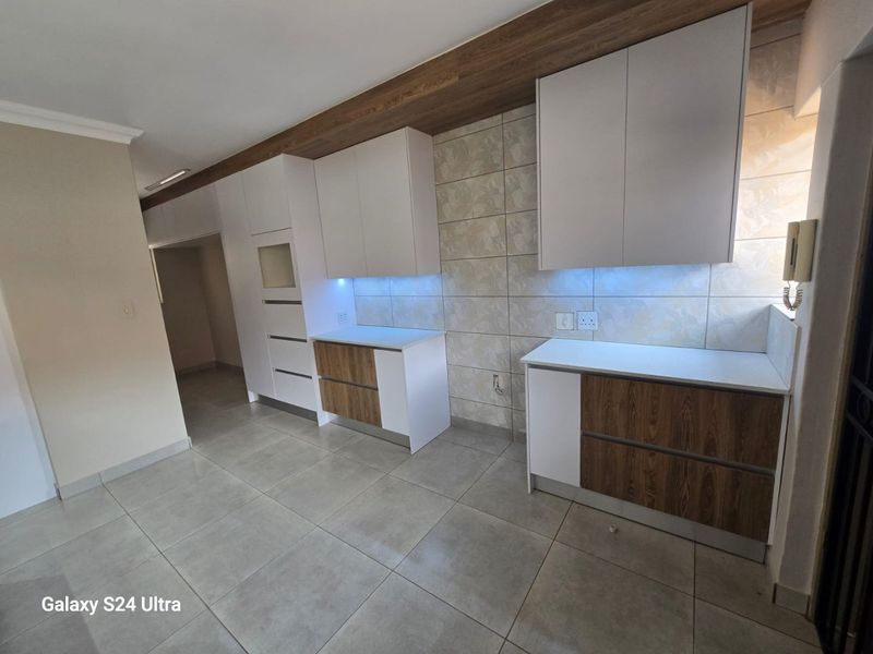 Modern kitchen featuring clean white and wood-grain cabinetry, stone countertops, tiled backsplash, and integrated under-cabinet lighting in a spacious, neutral setting.
