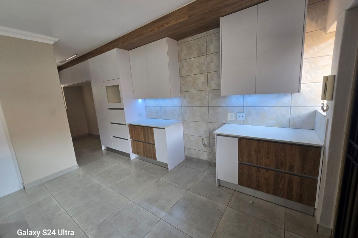 Modern kitchen featuring clean white and wood-grain cabinetry, stone countertops, tiled backsplash, and integrated under-cabinet lighting in a spacious, neutral setting.