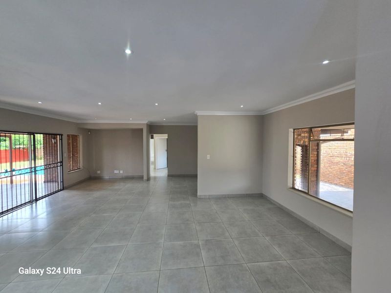 Spacious, open-plan living area featuring neutral tiled flooring, recessed downlighting, and large windows with security bars, offering a bright and versatile interior space.