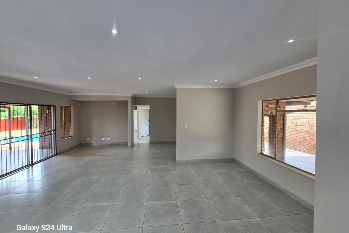 Spacious, open-plan living area featuring neutral tiled flooring, recessed downlighting, and large windows with security bars, offering a bright and versatile interior space.