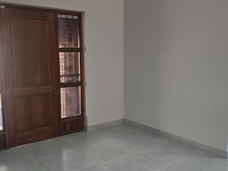 A bright and clean entrance area featuring a solid wooden front door with side light windows, tiled flooring, and neutral wall finishes.