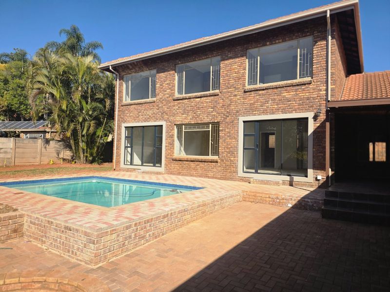 Rear view of a double-story brick house featuring a swimming pool, paved patio area, and large windows.