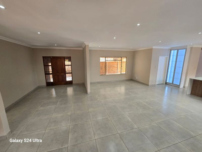 Spacious open-plan living area featuring neutral tiled flooring, recessed downlights, and ample natural light through large windows and a sliding glass door.